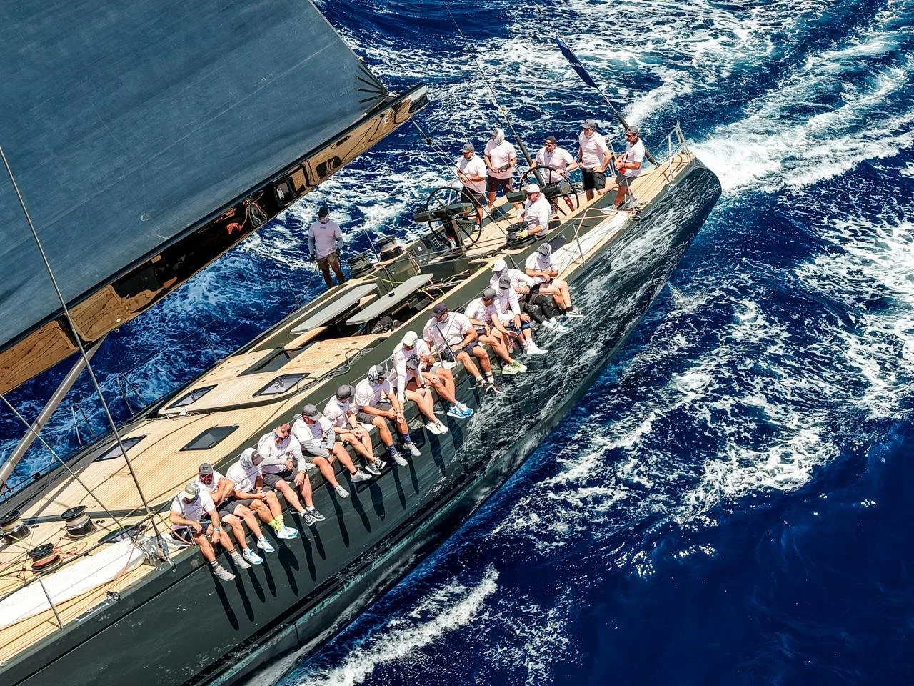 A yacht with a crew of people sitting on the edge, sailing on the open ocean with deep blue water and waves.