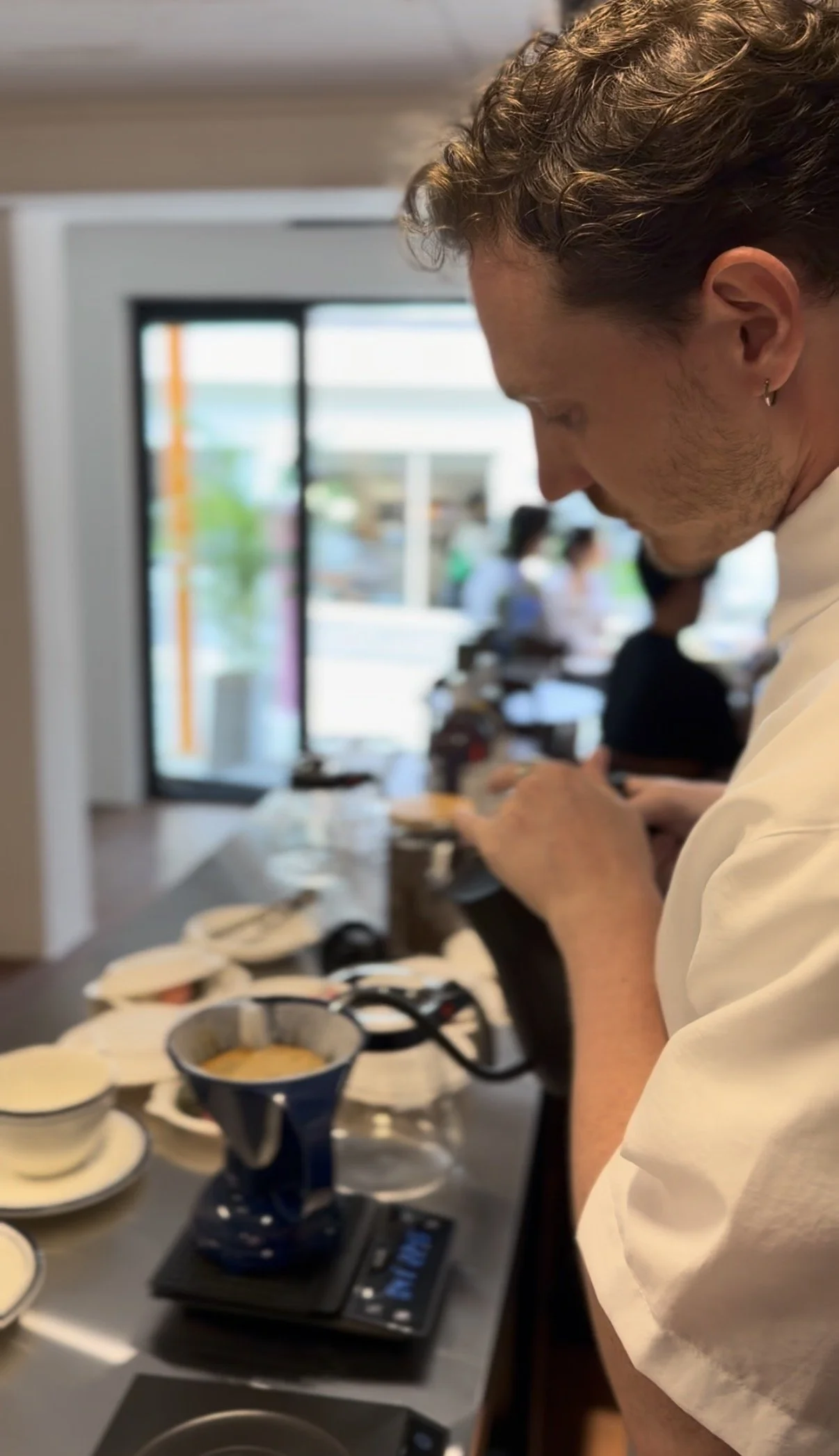 카페 또는 레스토랑에서 사람은 전기 커피 그라인더로 커피 원두를 갈고 있으며, 앞에는 디핑용 커피 드립 쉐이퍼와 액체가 담긴 컵이 놓여 있음.