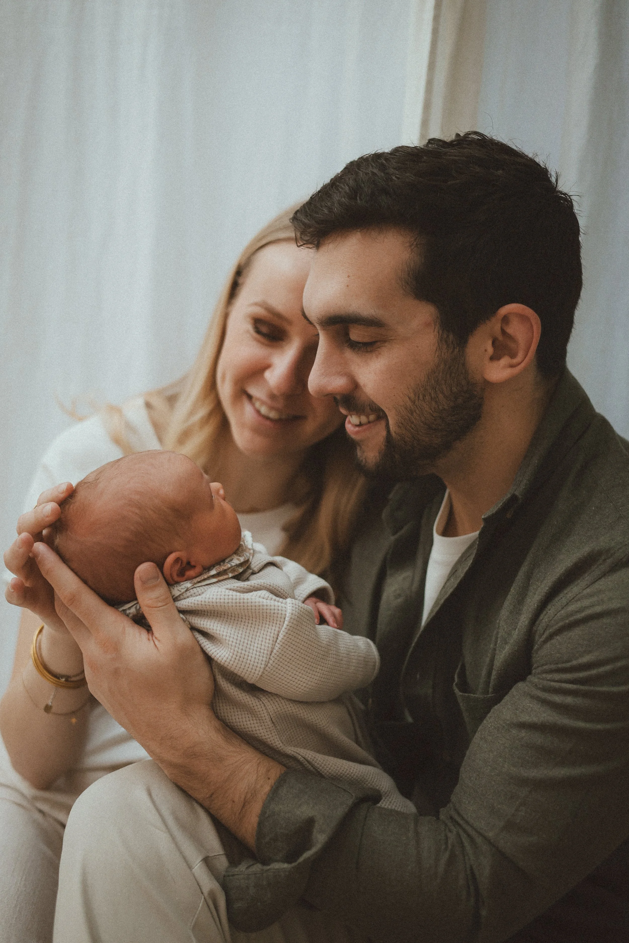 Un couple souriant tient un bébé, créant une scène chaleureuse et affectueuse.
