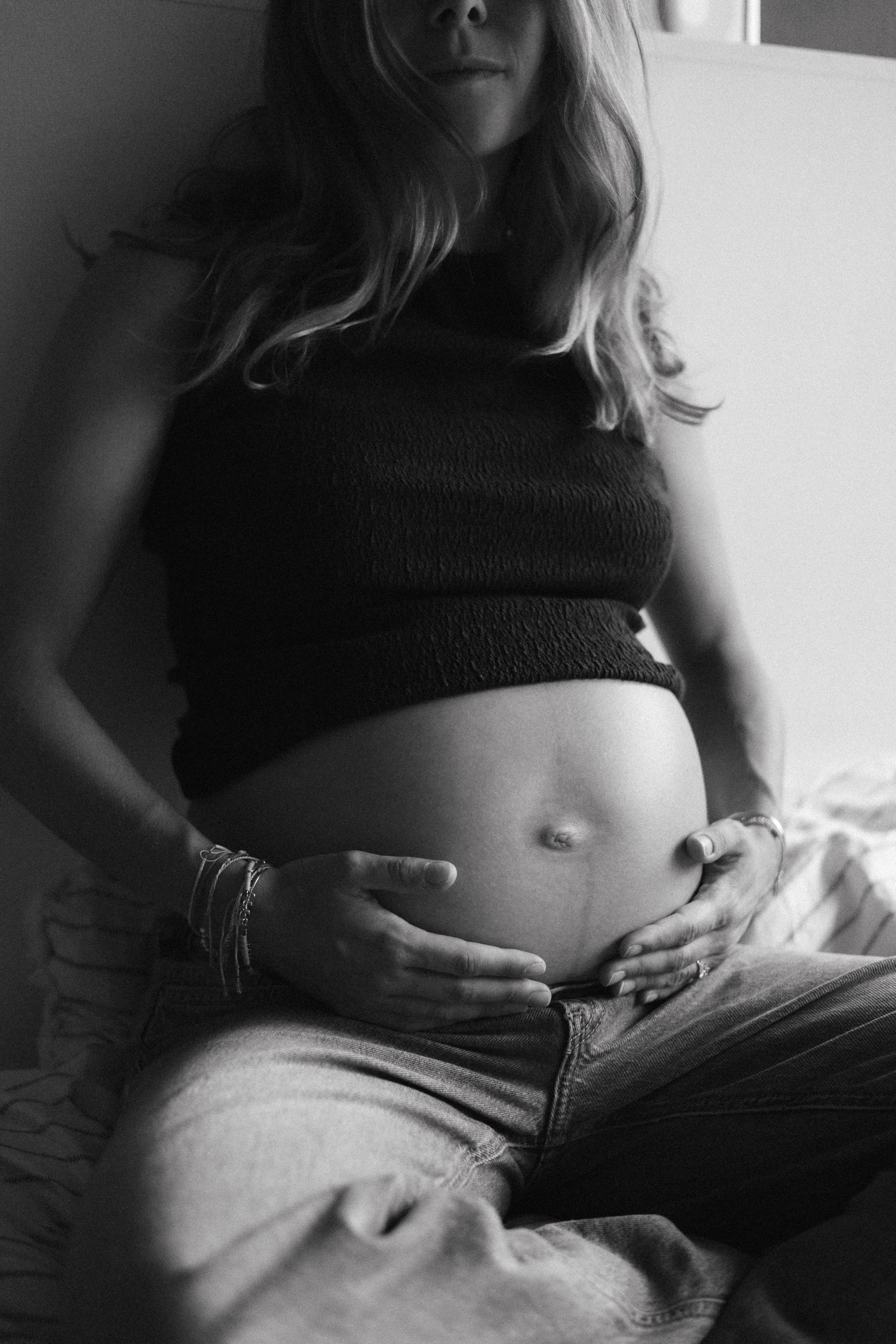 Une femme enceinte tenant son ventre avec ses mains, portant un haut noir, la photo est en noir et blanc.