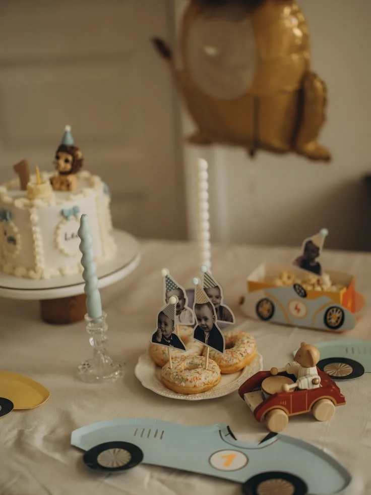 Table d'anniversaire avec gâteau, cupcakes, décorations, ballon en forme de voiture, et petits accessoires pour enfants.