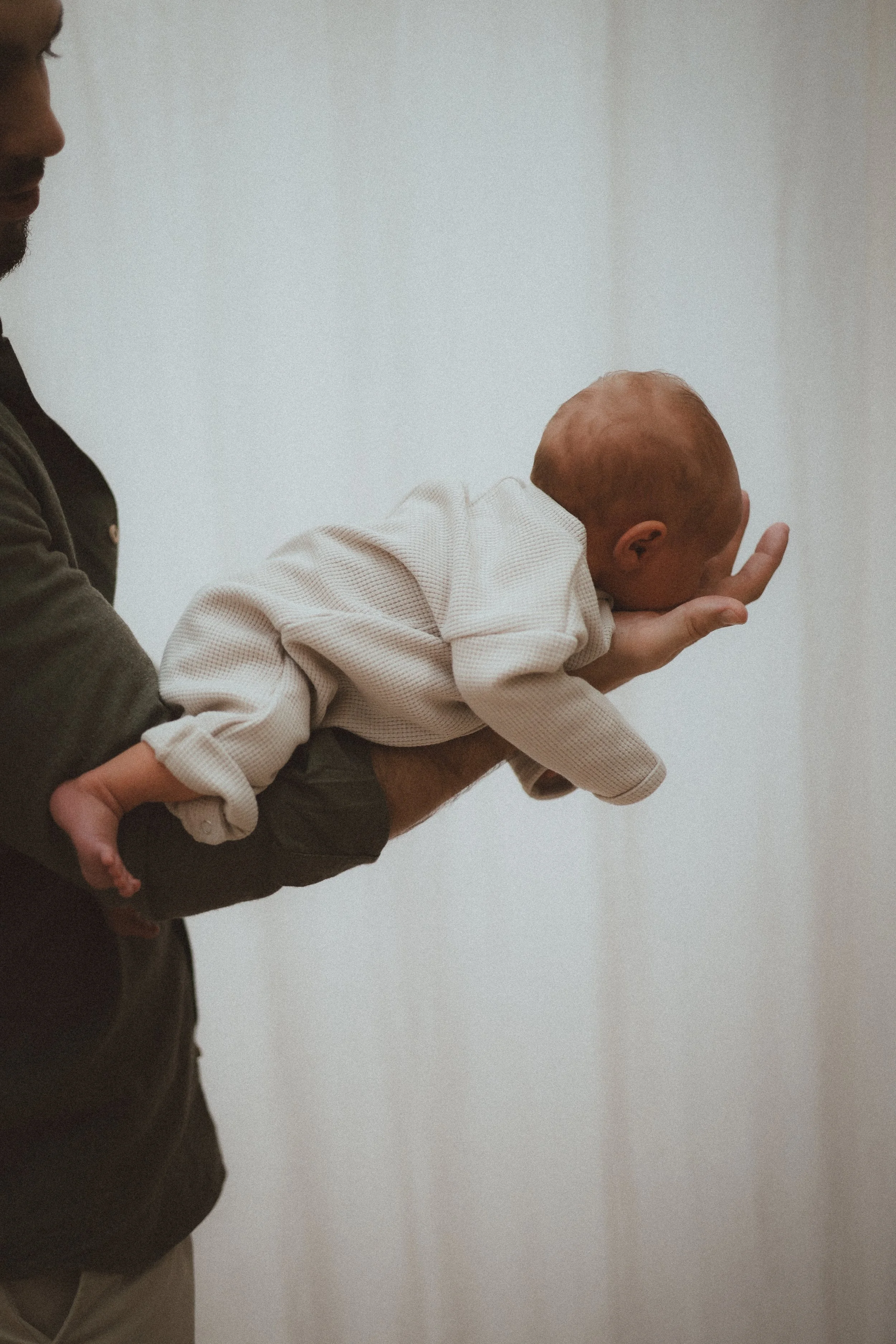 Un adulte tenant un bébé allongé sur son bras contre un mur blanc.