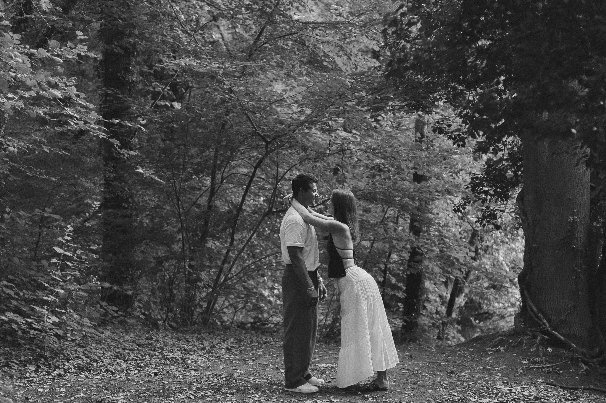 Un couple marchant dans une forêt, en regardant dans les yeux, partageant un moment intime, en noir et blanc.