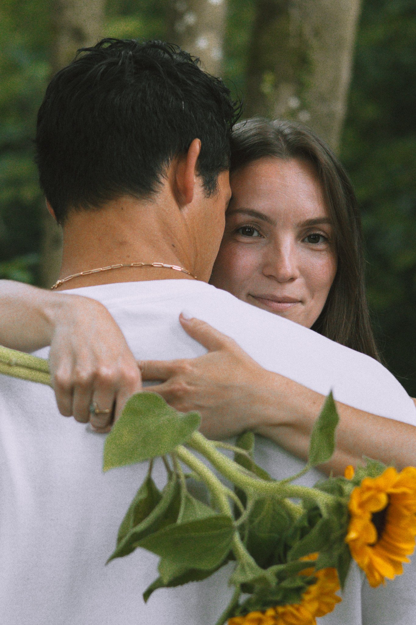 Un couple s'embrasse tendrement dans un contexte naturel, avec des plantes et des fleurs jaunes en premier plan.