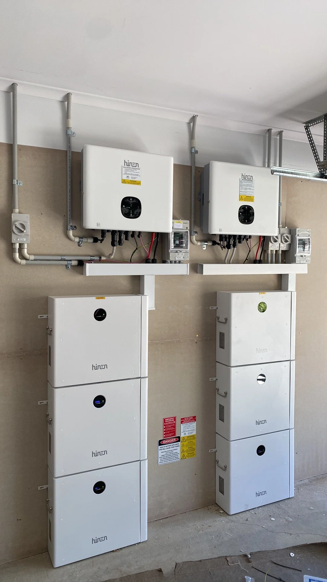 Batteries and inverters installed on a beige wall in a utility room.
