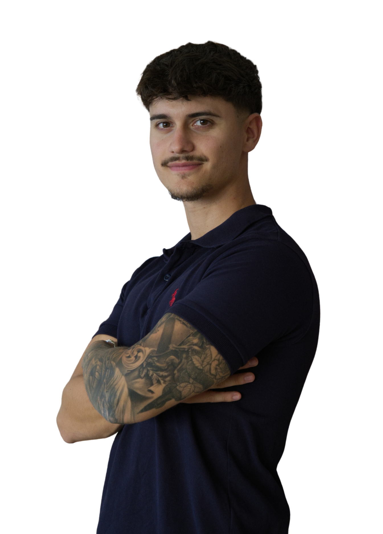 Ein junger Mann mit braunen, kurz geschnittenen Haaren, Tattoos am rechten Arm, trägt ein dunkelblaues Polo-Shirt und steht mit verschränkten Armen, lächelnd, vor schwarzem Hintergrund.