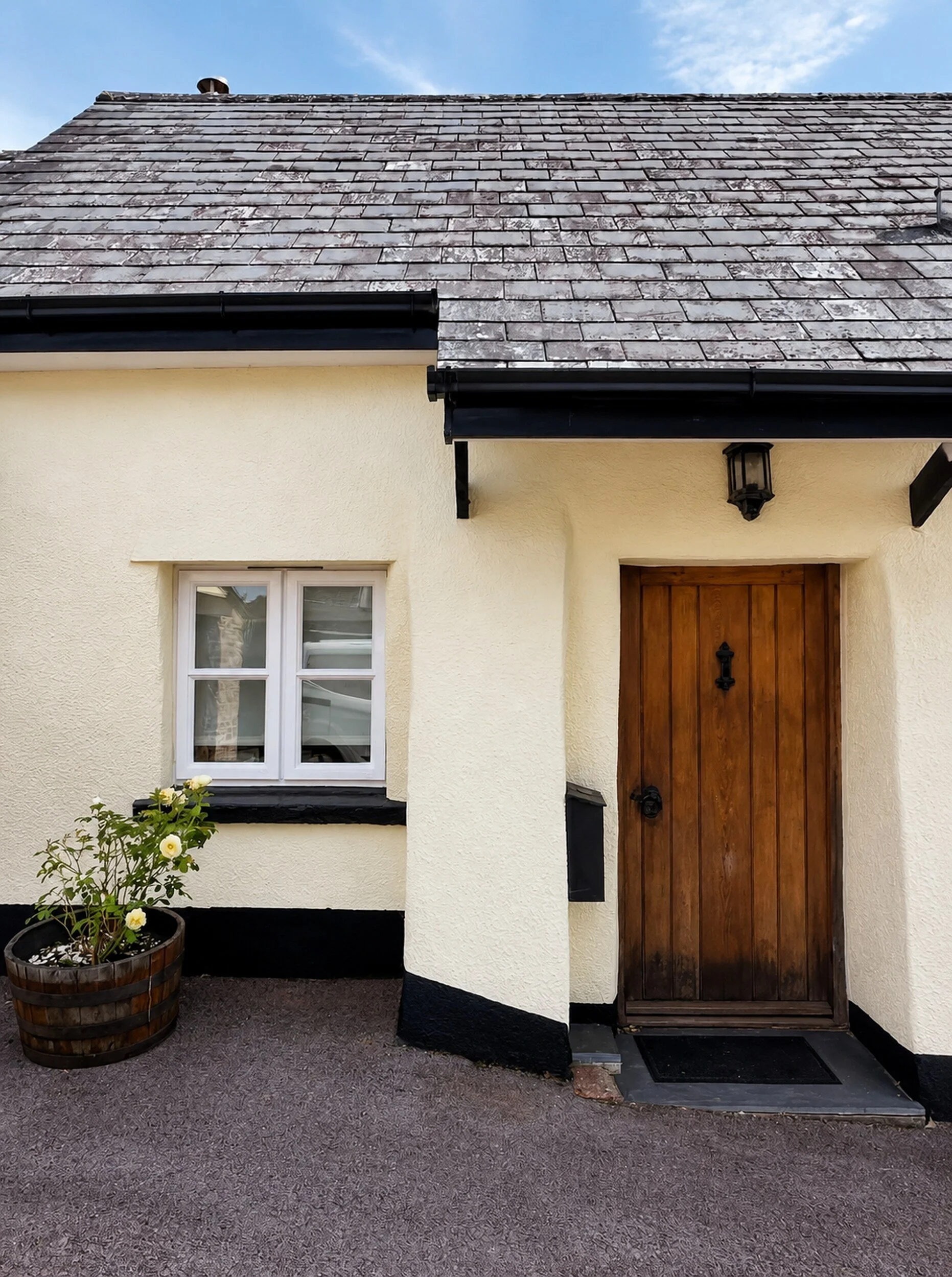Cottage exterior painted Cornish cream with black lower masonry and white-painted windows.