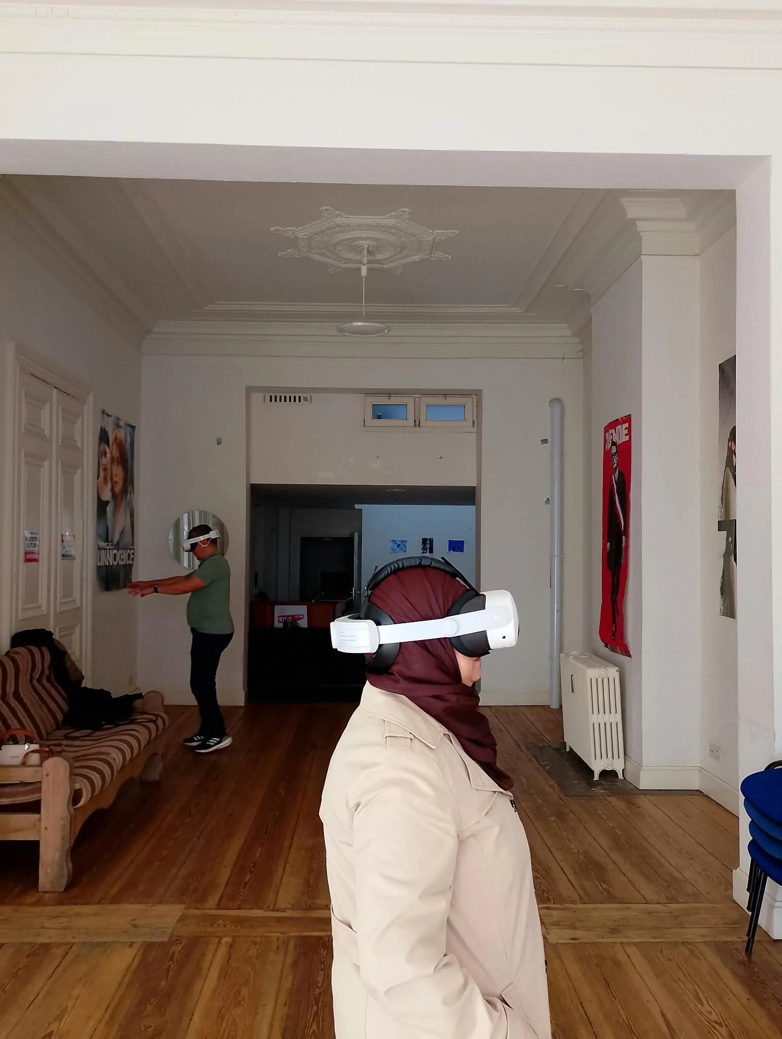 Deux personnes portant des casques de réalité virtuelle dans une pièce avec mobilier en bois, posters sur les murs et un plafond orné.