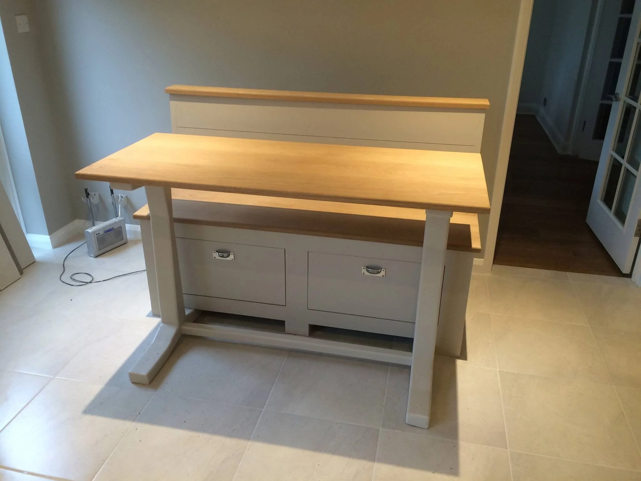 A white kitchen island with a wood top, drawers, and cabinets, situated on a tiled floor. A heater and electrical cord are visible on the left.
