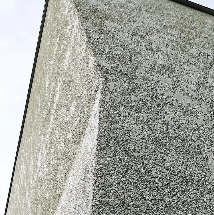 Close-up of a corner of a building with textured exterior wall surfaces in light and dark gray colors.