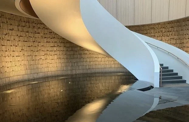 Modern interior with a curved white staircase, brick wall, and a pool of water reflecting the scene.