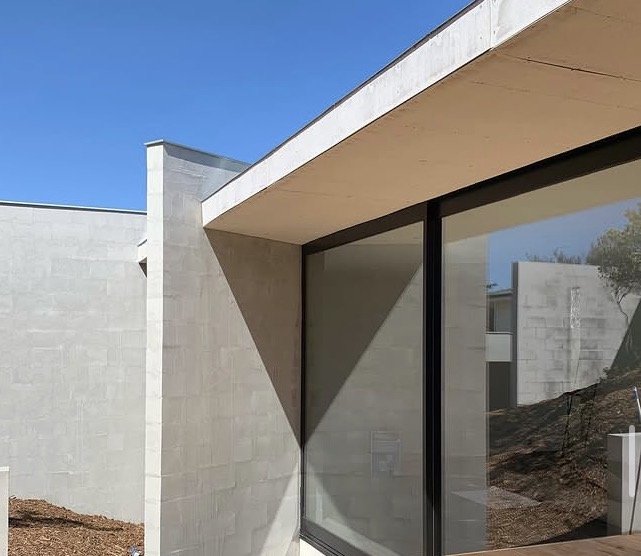 Close-up of modern building exterior with concrete walls, large glass window, and overhanging roof.