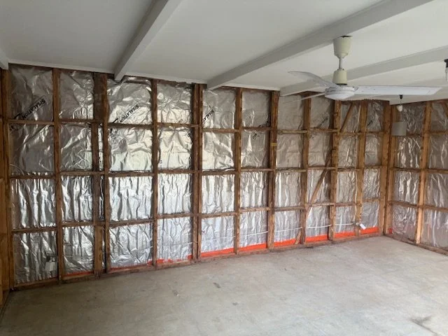 An unfinished room with exposed wall framing and insulation. The ceiling has a ceiling fan and a light fixture.