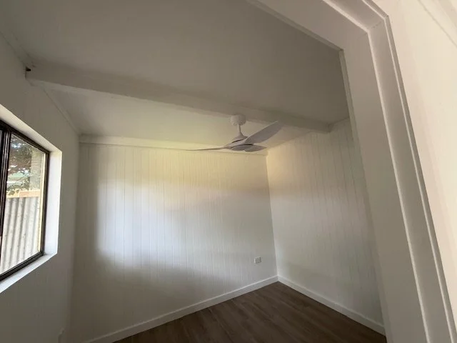 Empty room with white walls, a window on the left, a ceiling fan, and wood flooring.