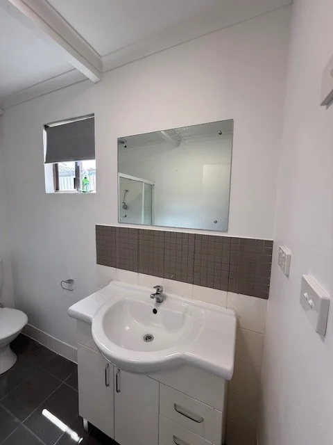 Bathroom with a white sink vanity, mirror, small window, and a toilet.
