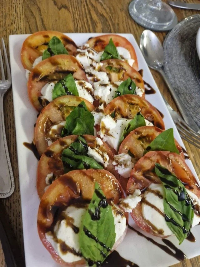 Plateful of Caprese salad with tomato slices, mozzarella, fresh basil leaves, and balsamic glaze