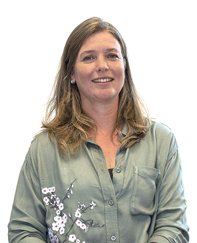 Een vrouw met bruin haar die glimlacht, zittend in een groene blouse met bloemenpatroon.