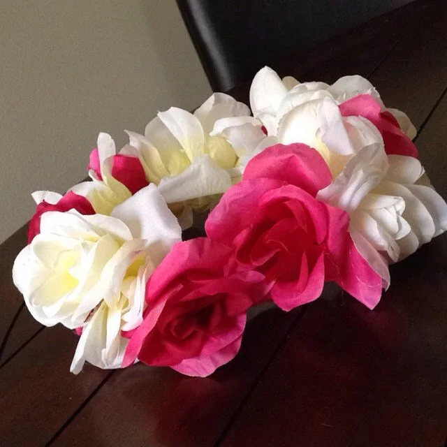 A floral lei made of white and pink artificial roses on a dark wooden surface.
