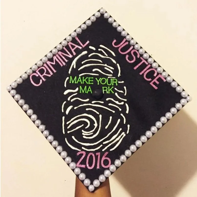 Graduation cap with a fingerprint design and words 'Criminal Justice 2016' in pink, and 'Make Your Mark' in green, decorated with white pearls around the border.