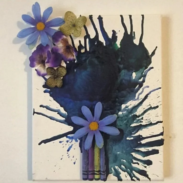 A creative artwork featuring a butterfly made from ink splashes, decorated with real flowers and butterflies, and crayons at the bottom.