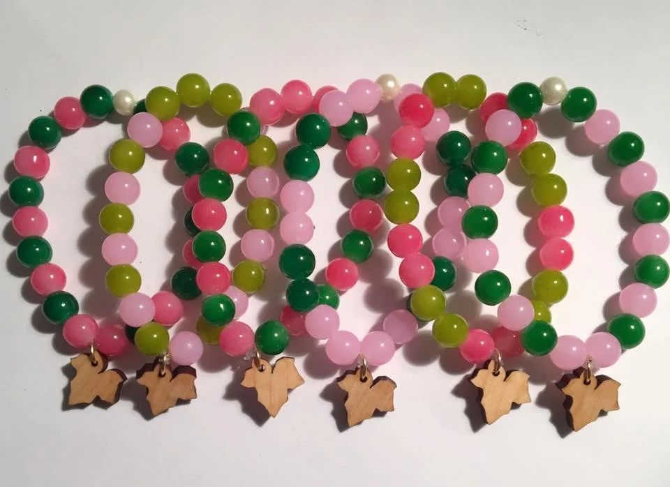 Colorful beaded necklaces with small wooden Texas shape charms laid out on a white surface.