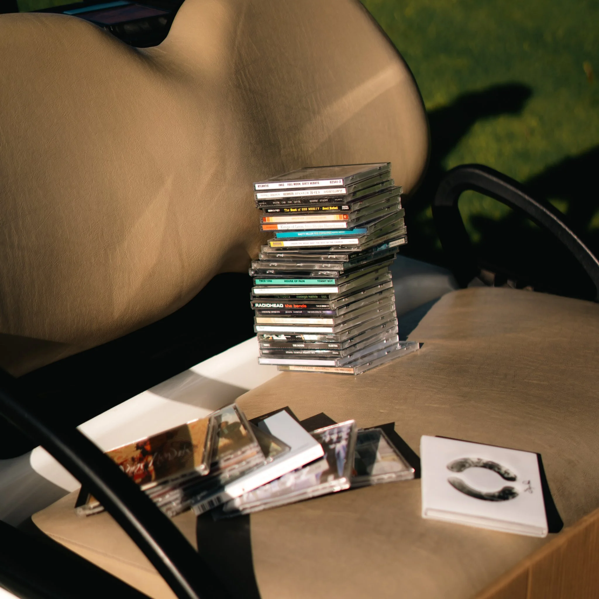 Stack of CD cases on a beige table, with a black and white album cover in the foreground and a green grassy background.
