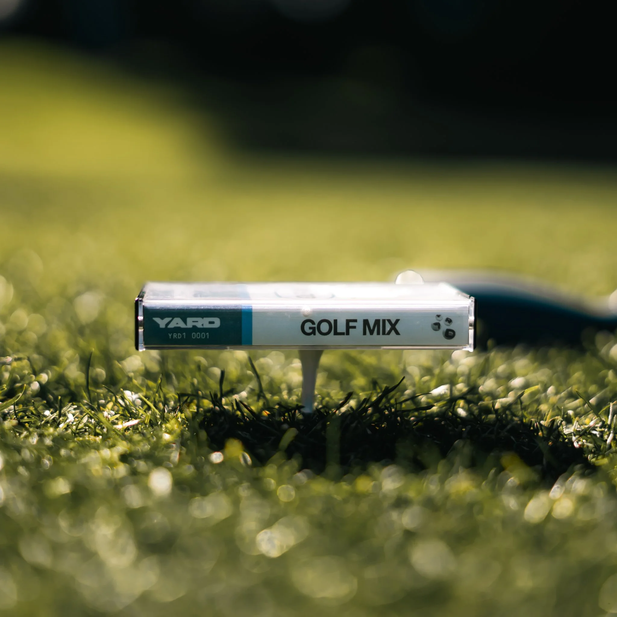 Close-up of a transparent box labeled "Golf Mix" placed on green grass, with blurred background of a golf course.