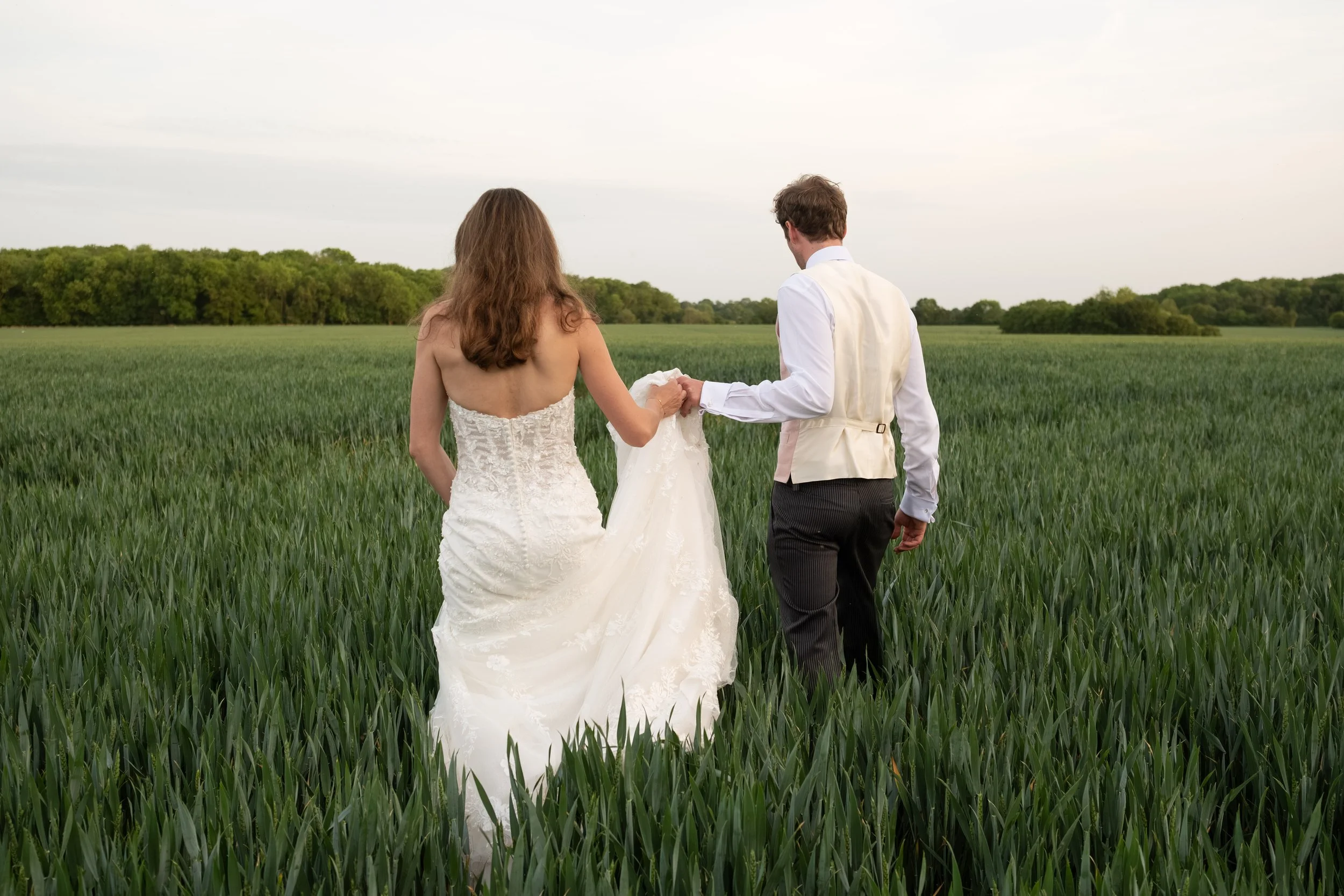 A bride and groom walk hand in hand through a green field during their outdoor wedding ceremony.