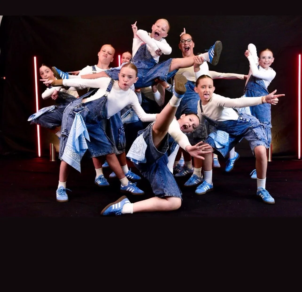 Group of children in denim outfits posing playfully in front of a black backdrop with red neon lights.