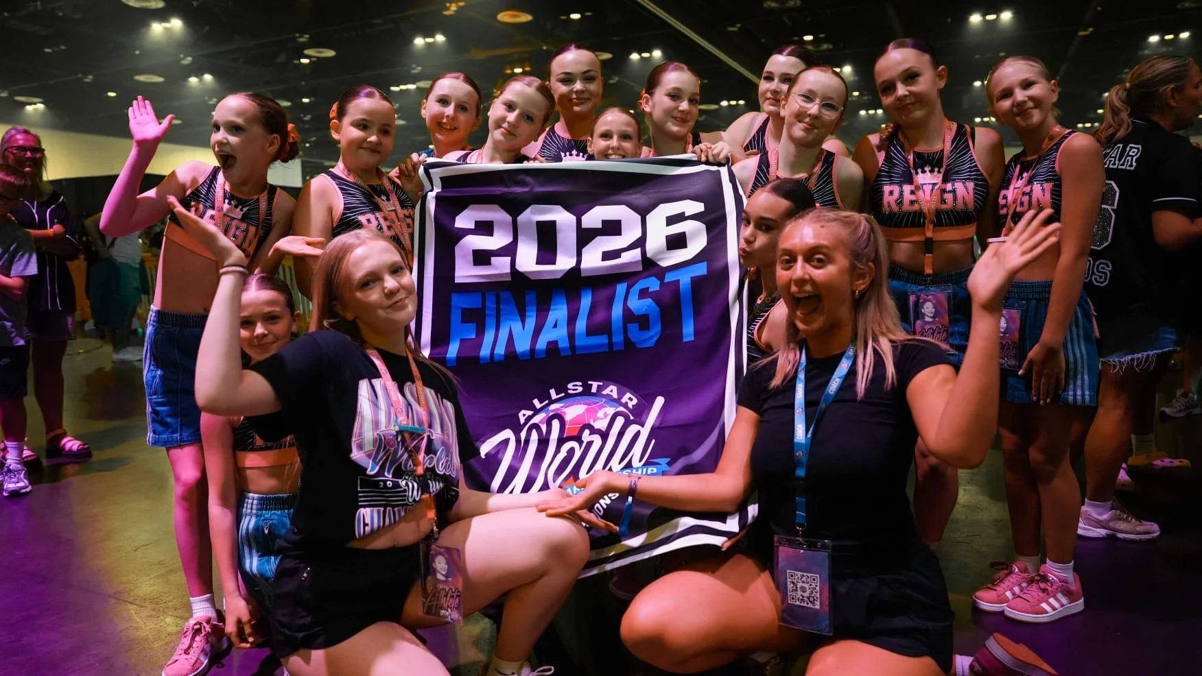 Group of young girls celebrating at a cheerleading competition, holding a banner that says '2026 Finalist' and 'All Star World'.