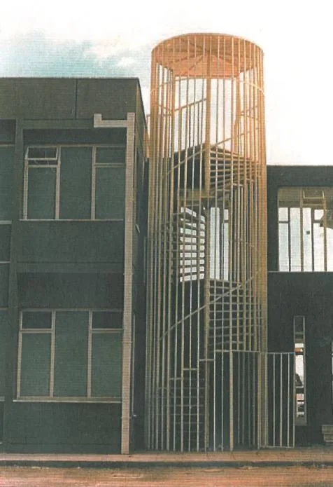 Exterior view of a multi-story building with a cylindrical metal staircase structure on the side.