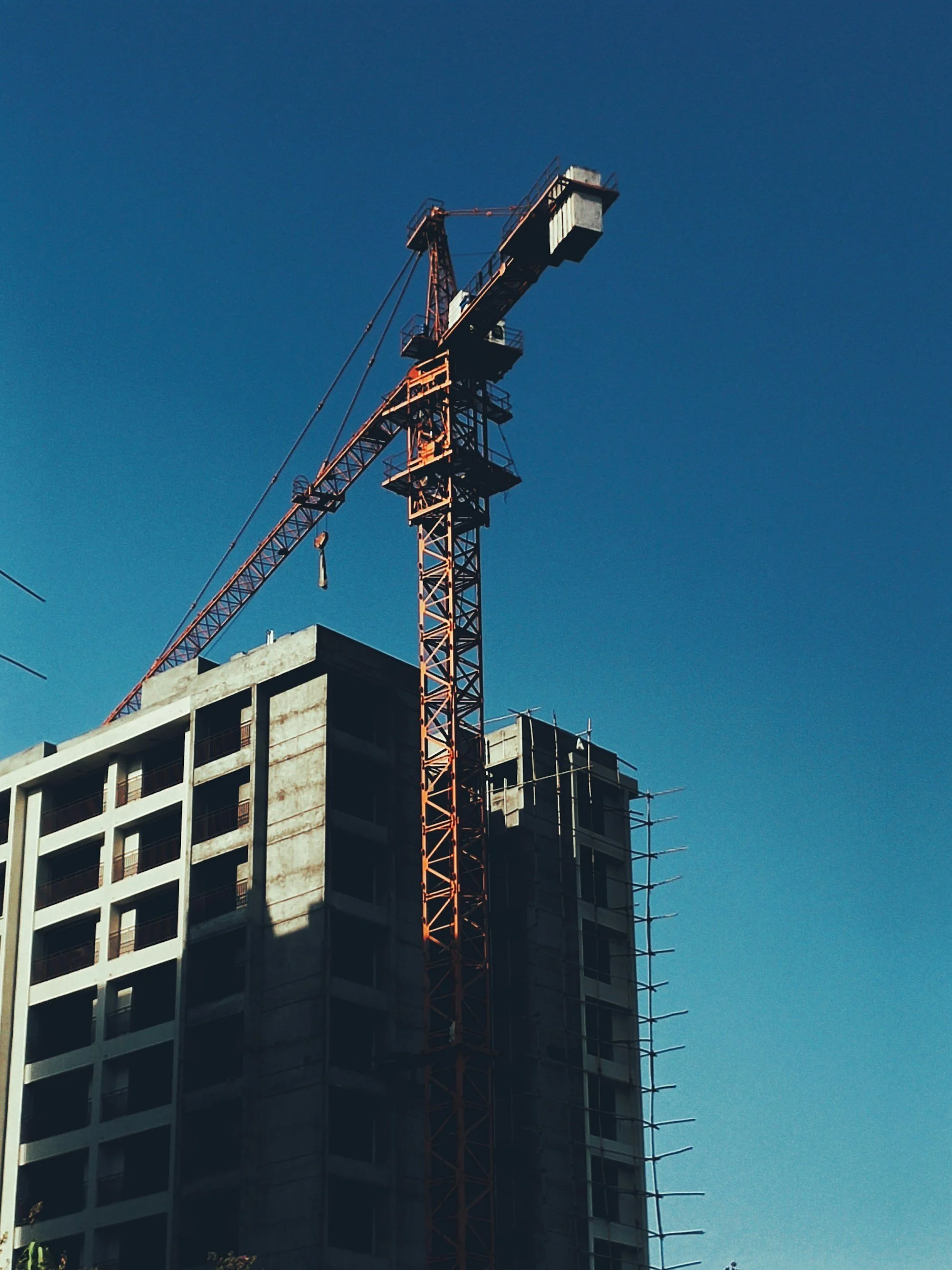 A construction crane is on top of a tall building under construction, against a clear blue sky.