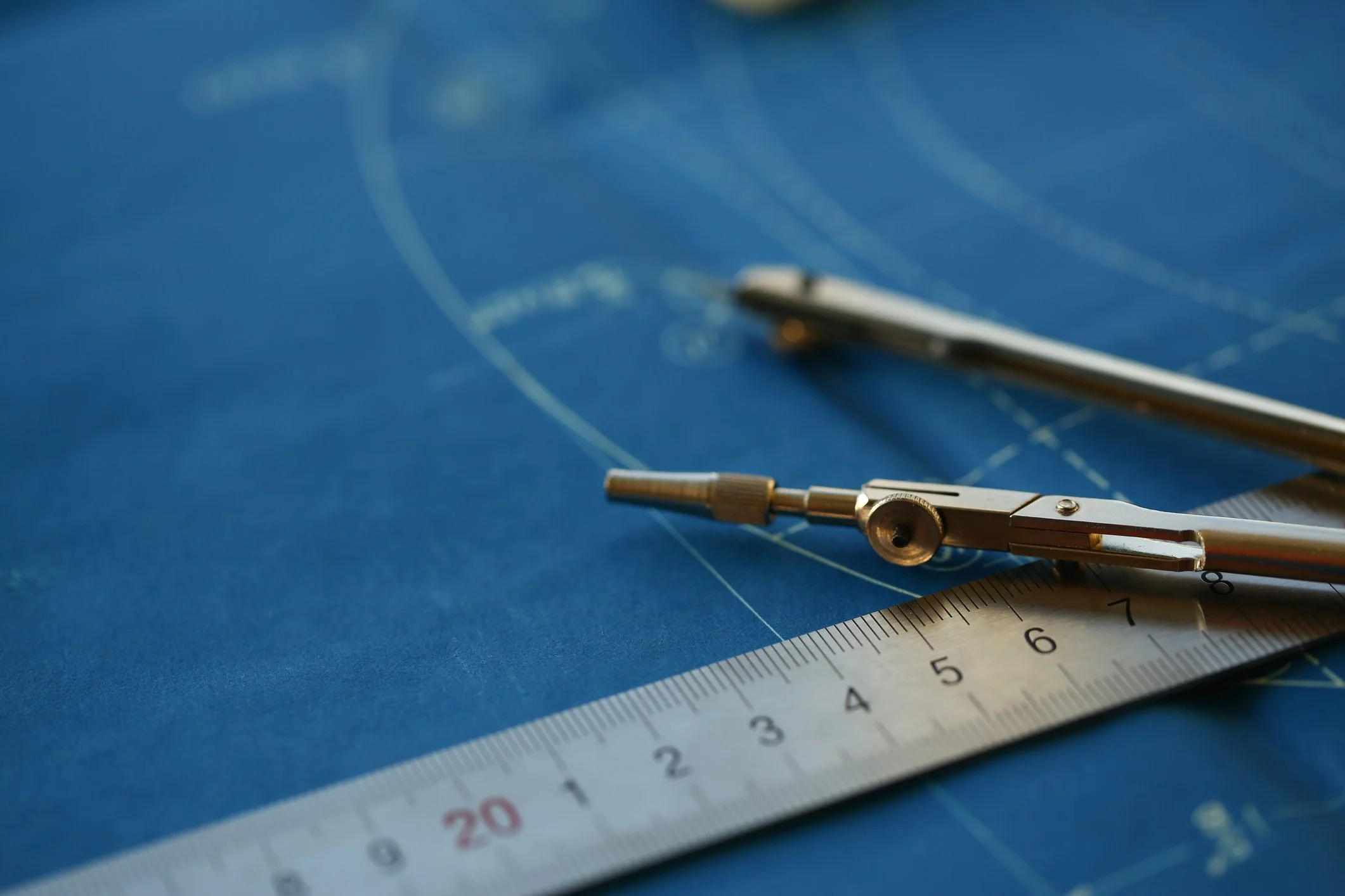 A metal compass, a ruler, and a blue blueprint with engineering lines and measurements.