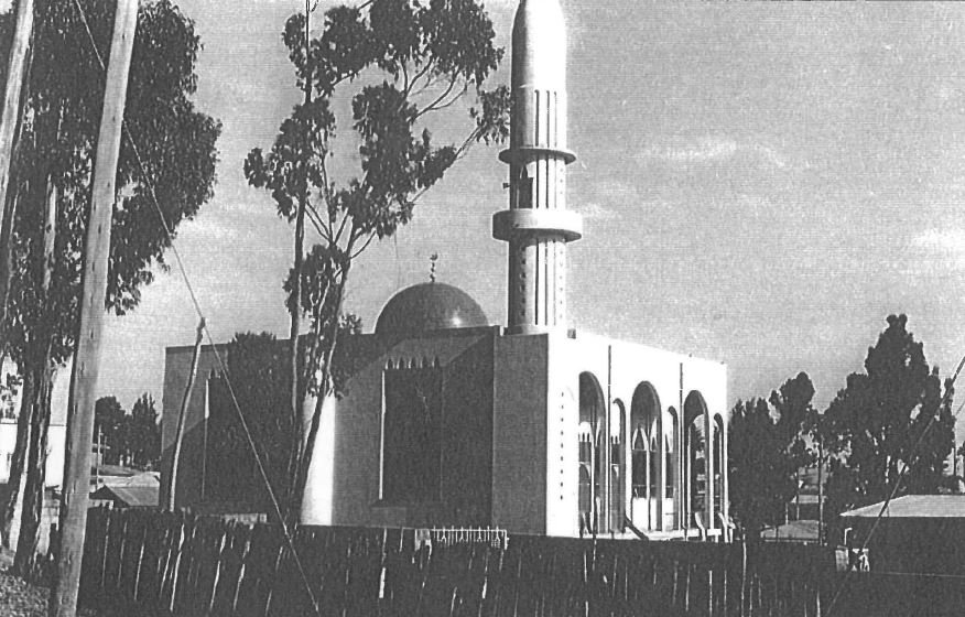 Black and white photo of a building with Islamic architectural features, including arches and a dome, surrounded by trees.