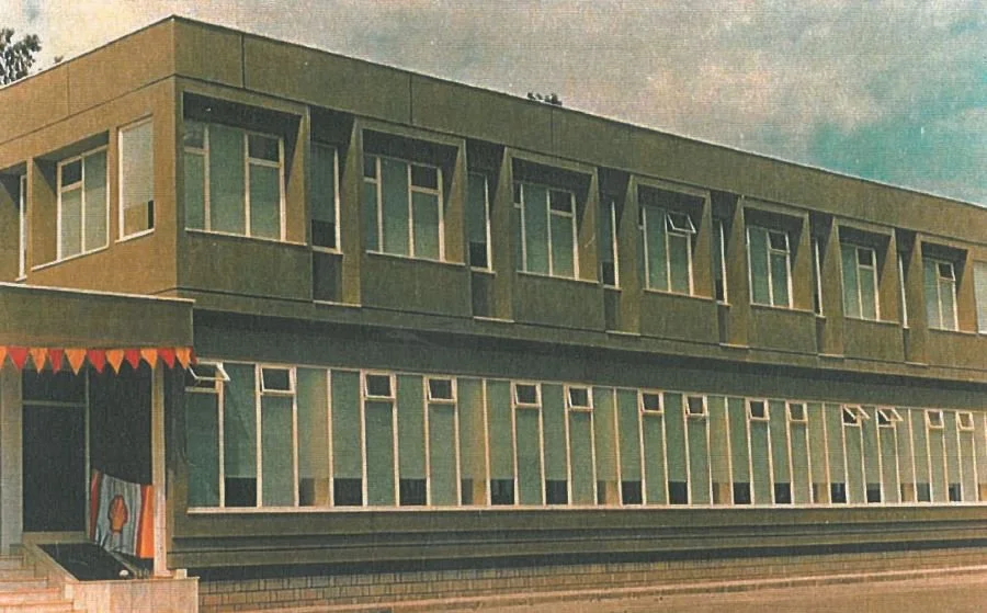 A two-story modern building with numerous windows, painted in shades of green and tan, with an awning and bunting decorations outside.