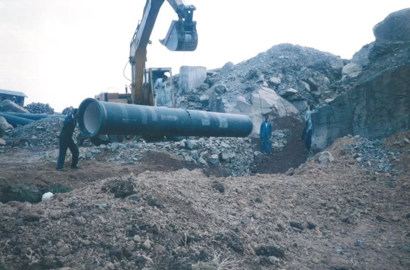 Construction workers and equipment working on installing or repairing a large pipeline in a rocky, dirt area