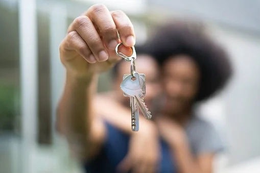 Person holding out a keychain with two keys towards the camera, blurred background.