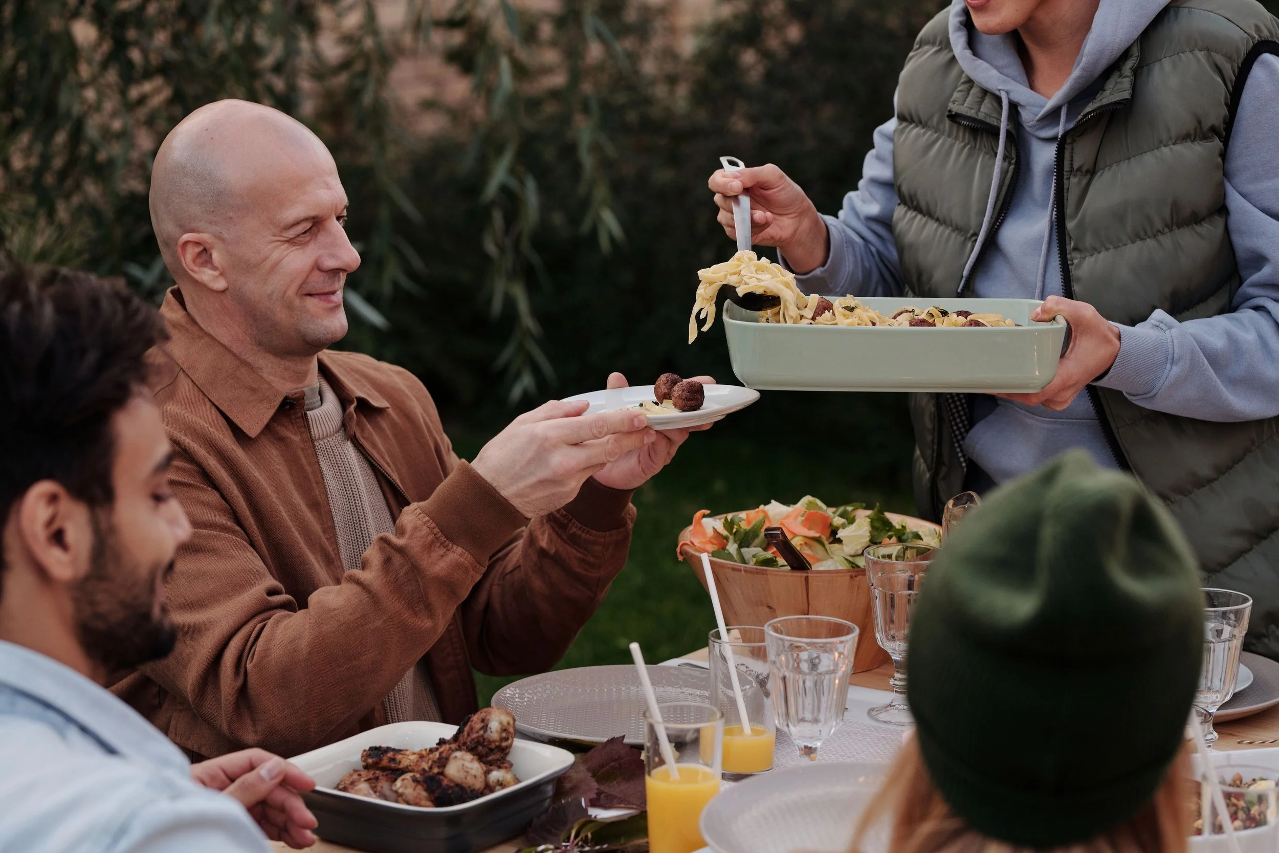 People enjoying outdoor meal with food and drinks on a table