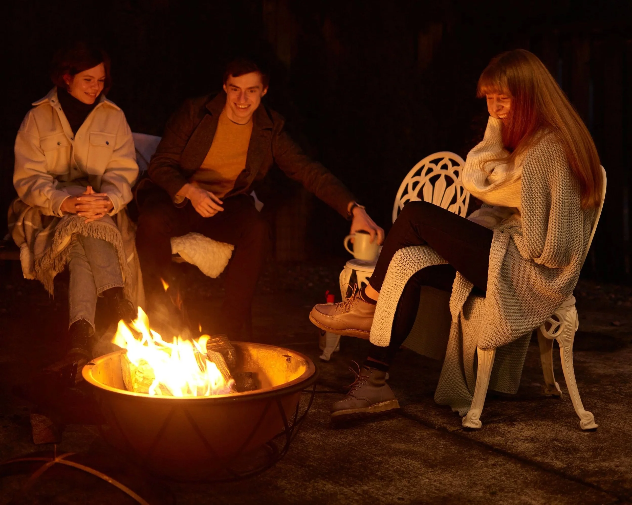 Four people sitting around a fire pit outdoors at night, smiling and enjoying their time together.