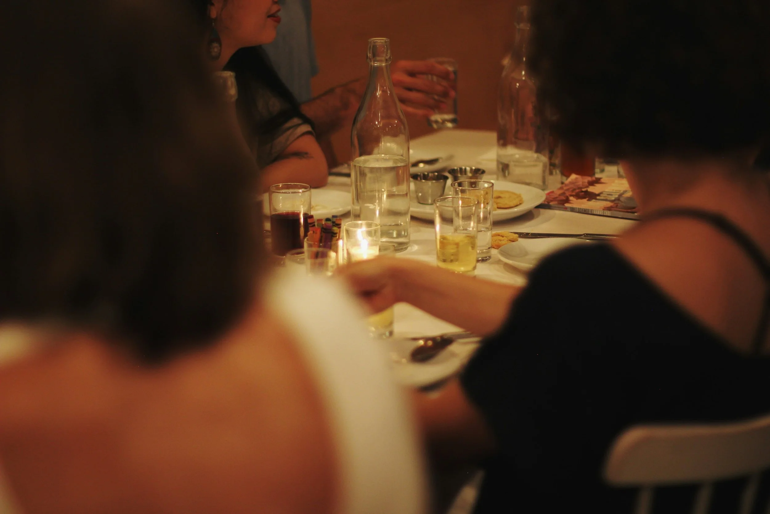 People sitting around a table with drinks and snacks at a dimly lit gathering or party.