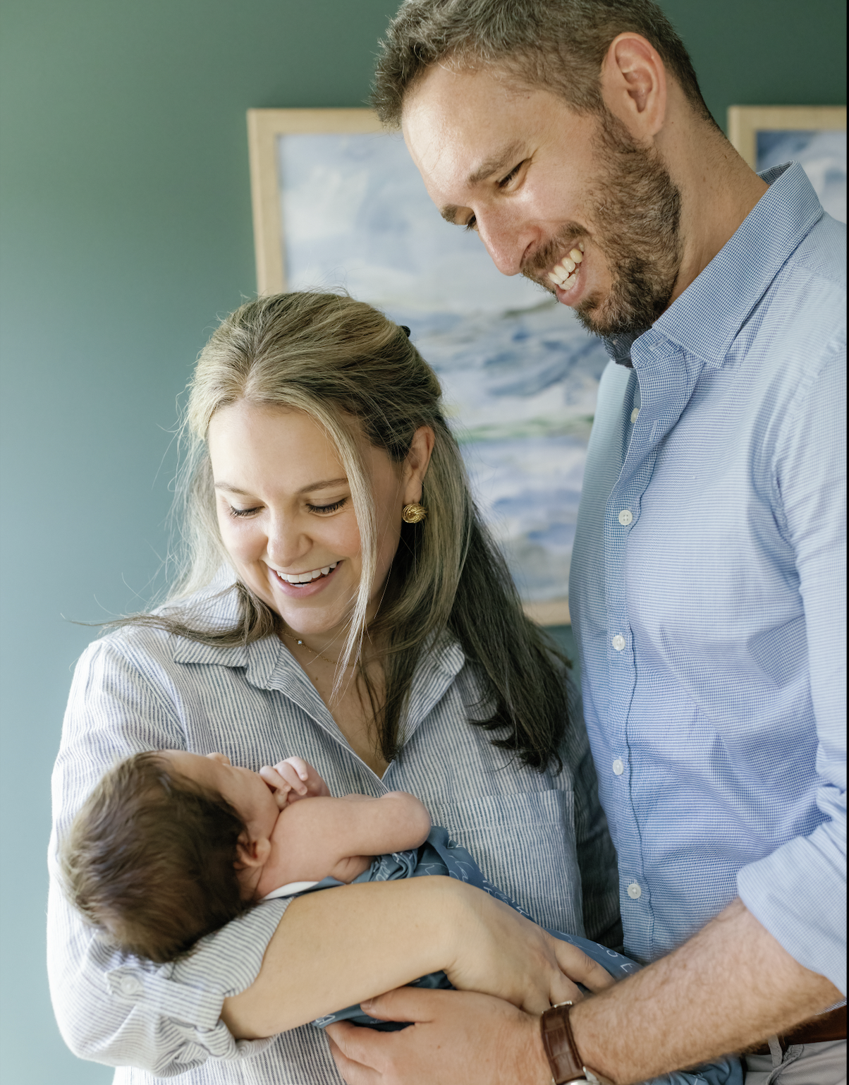 A happy couple holding a newborn baby in a hospital room, smiling and gazing lovingly at the infant.