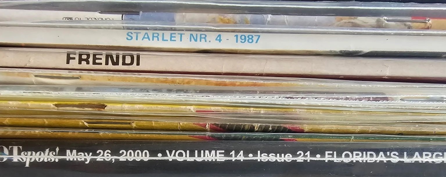 Stack of magazines or newspapers with visible titles including "STARLET NR. 4 - 1987", "FRENDI", and part of a sign from May 26, 2000.