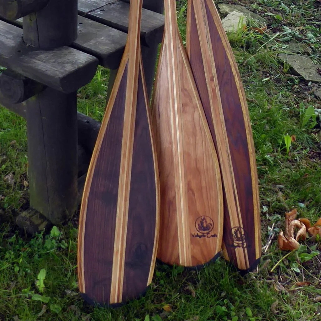 Three wooden kayaks with striped patterns lean against a wooden bench on grassy ground.