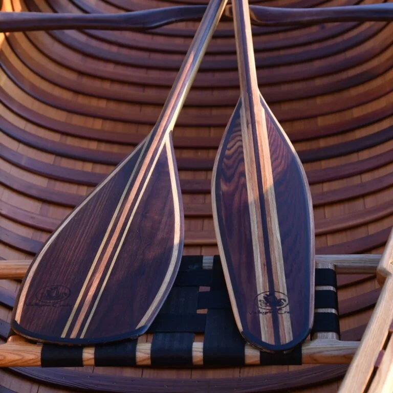 Two wooden paddles with striped patterns resting on a wooden chair with a curved slatted back.