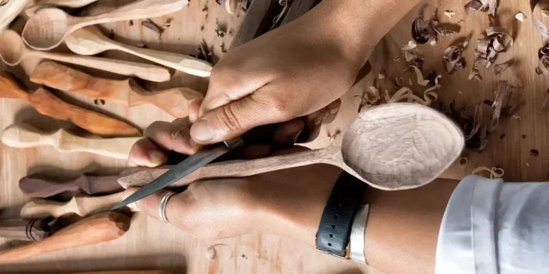 A person carving wood with a chisel, surrounded by wood shavings.