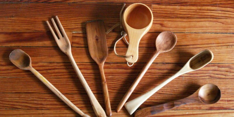Several wooden kitchen utensils including spoons, a fork, and a mug, arranged on a wooden surface.