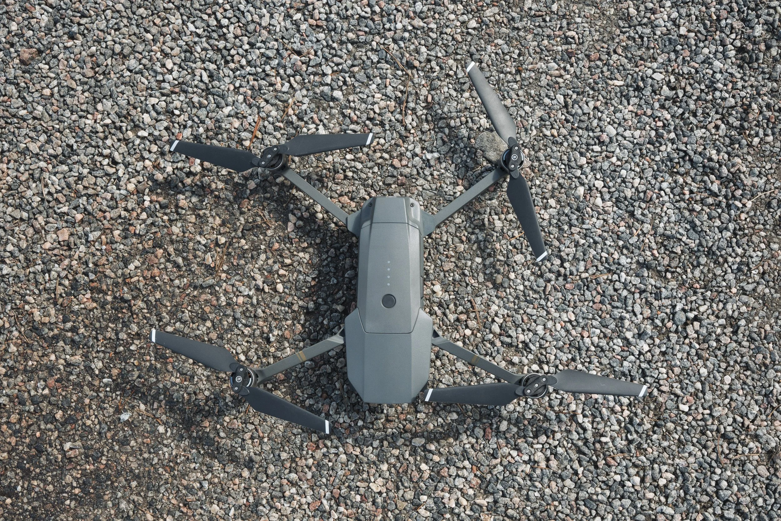 A drone with four propellers resting on a gravel surface.