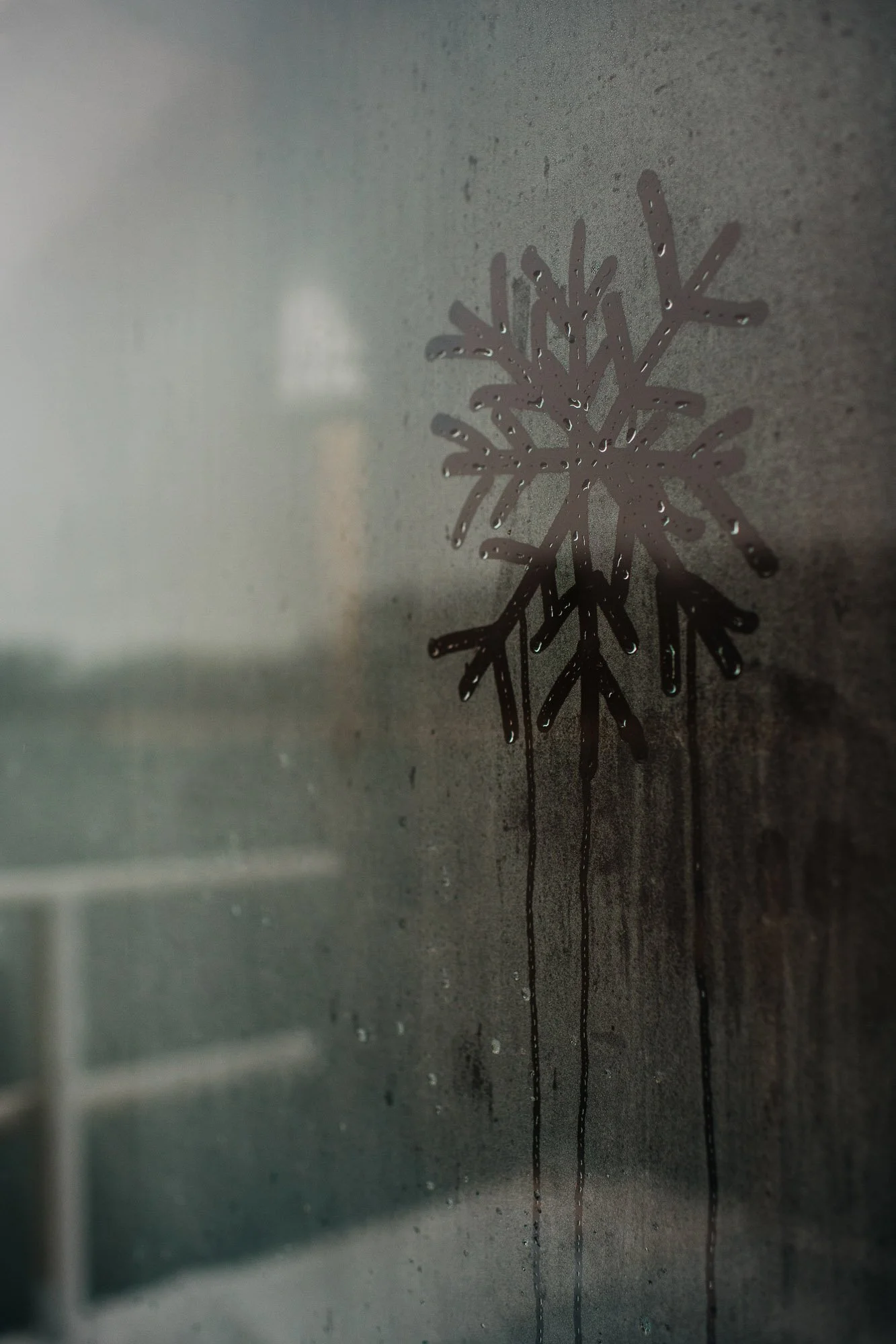 A close-up photograph of a snowflake-shaped decoration stuck on a foggy glass surface with water droplets and streaks.