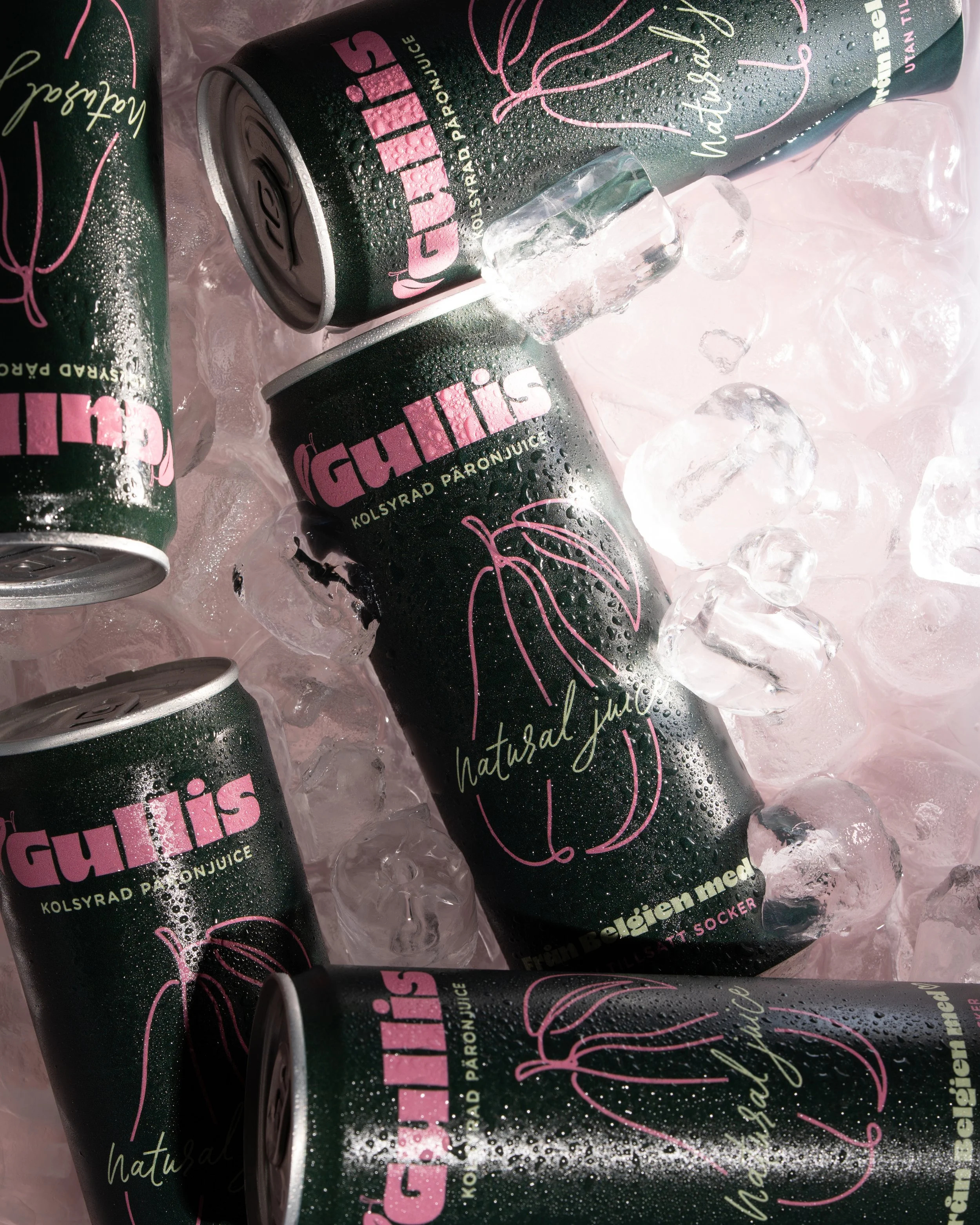 Several cans of a beverage with a black label, pink and gold text, and a pink outline of a flower or plant, resting on ice with condensation droplets visible on the cans.