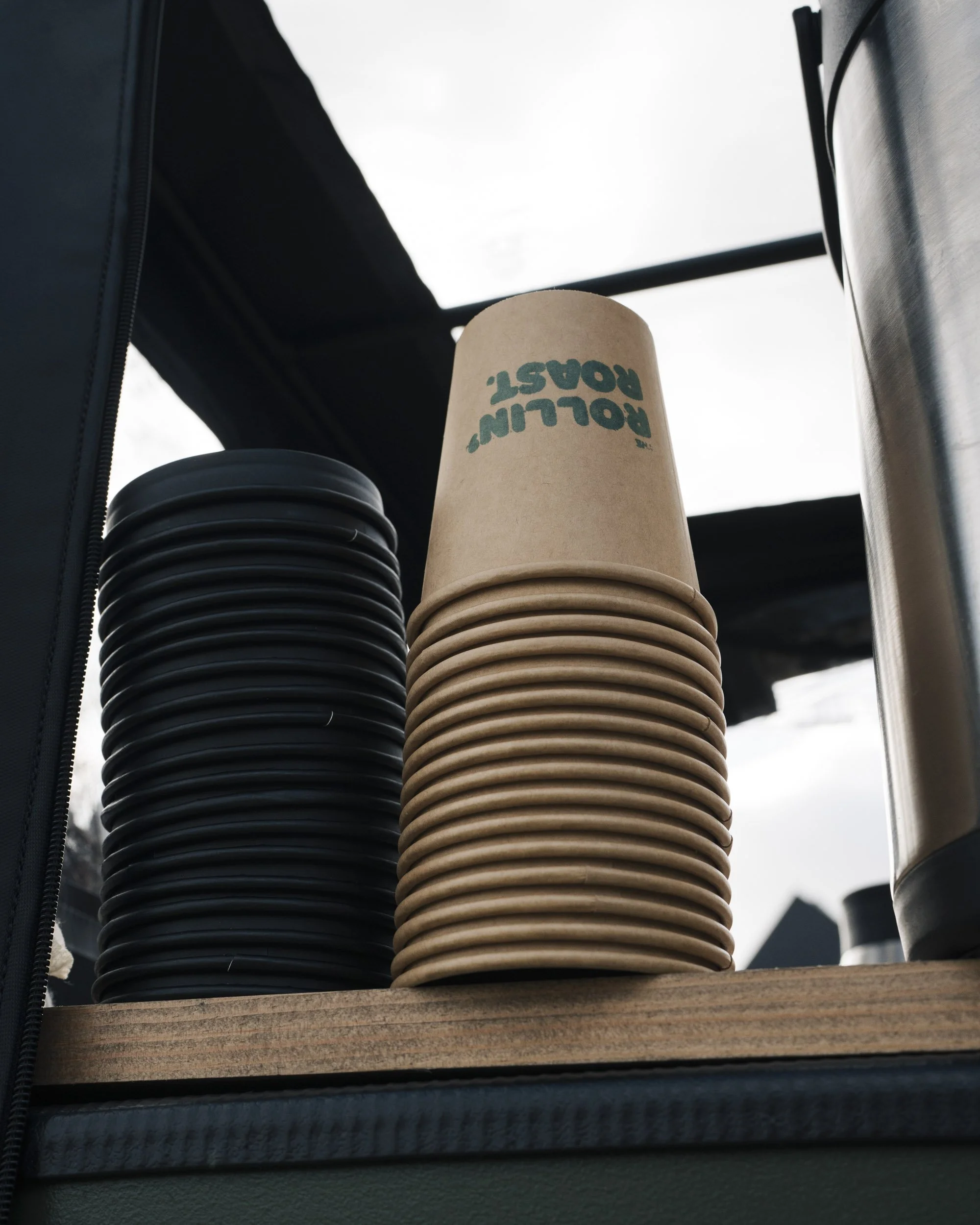 Stacked Starbucks coffee cups on a wooden shelf with a black plastic cup on the side.